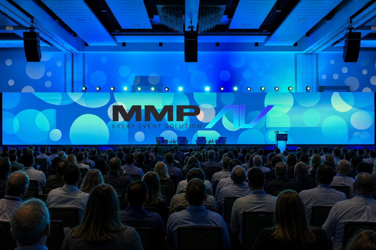 Sold-out corporate general session with full-width MMP AV curved LED wall, blue stage lighting, and audience facing the main stage