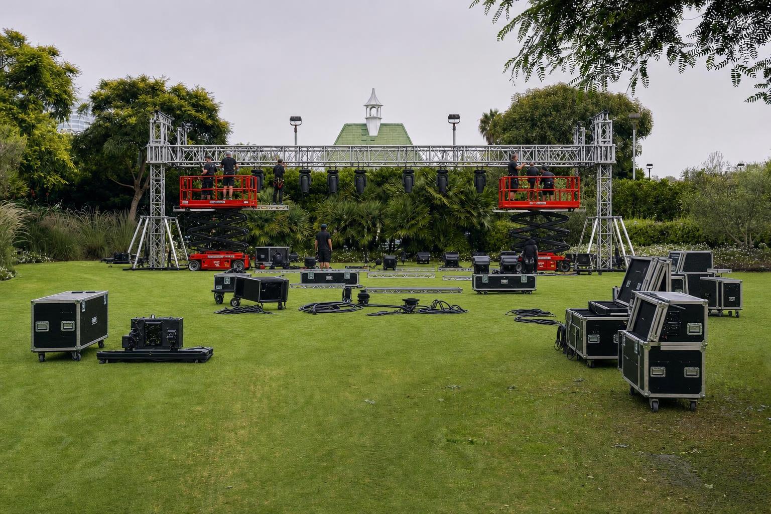 Lighting technicians on a genie lift pre-rigging aluminum truss and moving heads with road cases and DMX cable on the floor